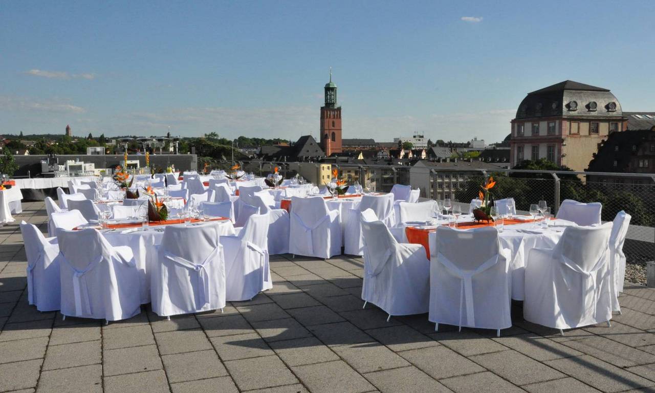 Festlich eingedeckte runde Tische auf der Dachterrasse des darmstadtiums. Im Hintergrund erkennt man die Evangelische Stadtkirche. Auf der Rechten Seite befindet sich das Darmstädter Residenzschloss.